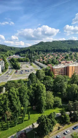 Výhled z mrakodrapu na zeleň, zlínské sídliště a zalesněné kopce v pozadí