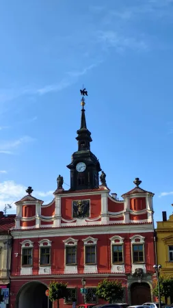 Červenobílá stará radnice v Chrudimi s hodinovou věžičkou a ozdobným štítem pod modrou oblohou