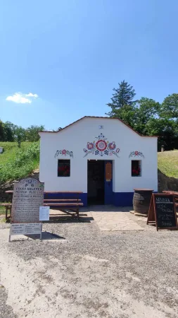 Bílý vinný sklípek s malovanými lidovými ornamenty, lavicemi a sudem na jižní Moravě