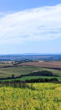 Rozlehlý výhled na pole a kopce jihomoravské krajiny pod modrou oblohou s mraky