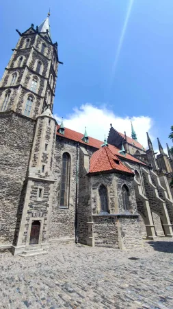 Gotický chrám svatého Bartoloměje s věží a červenou střechou apsidy pod modrou oblohou