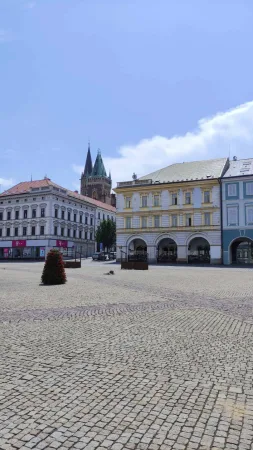 Dlážděné Karlovo náměstí v Kolíně s barevnými měšťanskými domy a gotickou věží v pozadí