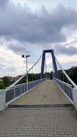 Pěší lávka s modrými pylony vedoucí přes řeku Labe v Kolíně pod zataženou oblohou