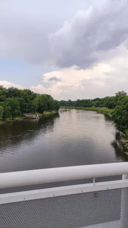 Řeka Labe obklopená zelení při pohledu z lávky v Kolíně za oblačného dne