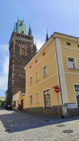 Gotická věž chrámu svatého Bartoloměje nad žlutým domem v uličce v Kolíně