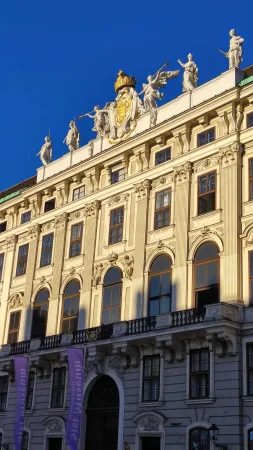 Zlacený erb a sochy na vrcholu fasády Hofburgu