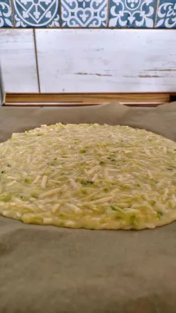 Cuketové těsto na pizzu rozprostřené na plechu s pečicím papírem, pohled z boku