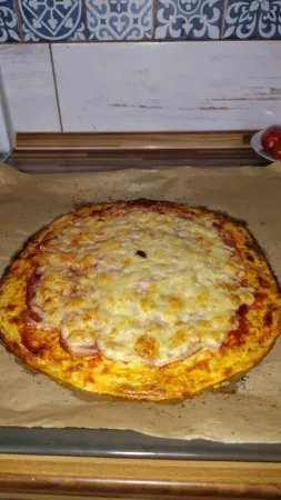 Hotová cuketová pizza s rozpečeným zlatavým sýrem a šunkou na pečicím papíře