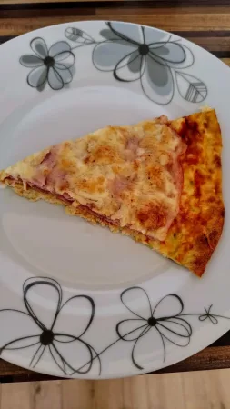 Kousek cuketové pizzy se šunkou a sýrem na bílém talíři s květinovým vzorem