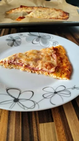 Trojúhelníkový kousek cuketové pizzy na talíři, zbytek upečené pizzy na plechu v pozadí
