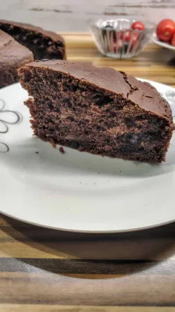 Krajíc cuketového koláče s čokoládou na talířku s květinovým vzorem, v pozadí miska rajčat.