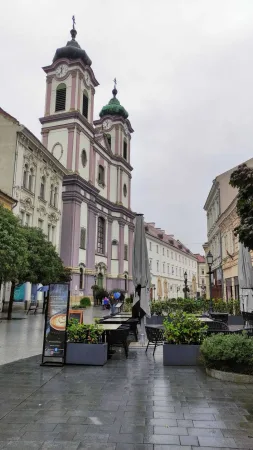 Fialová fasáda cisterciáckého kostela s dvěma zelenými věžemi tyčícími se nad náměstím