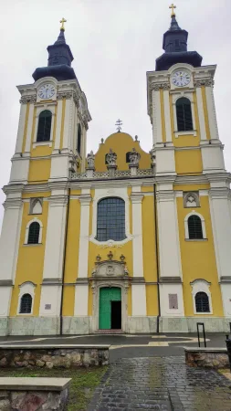 Žlutá fasáda kostela se dvěma věžemi a hodinami na věžích