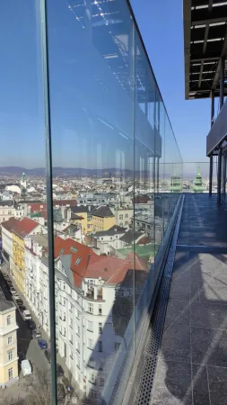 Výhled na barevné střechy vídeňských domů ze skleněné terasy