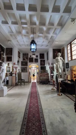 Dlouhá chodba galerie s červeným kobercem, obrazy a sochou
