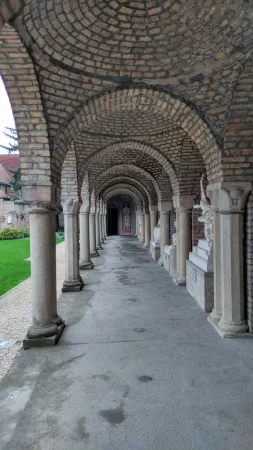 Klenutá cihlová chodba ambitu vedoucí k sochám v pozadí
