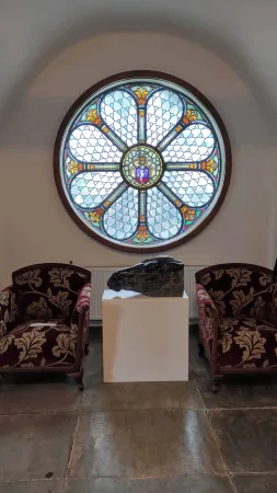 Kulaté vitrážové okno nad dvěma sametovými křesly