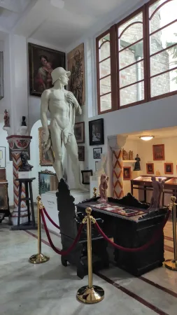 Bílá mramorová socha muže obklopená obrazy v interiéru galerie