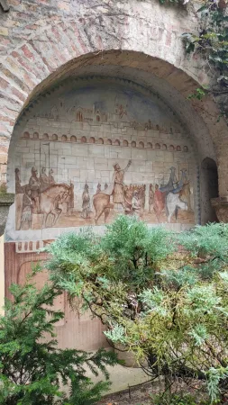 Reliéfní malba karavany velbloudů a jezdců pod cihlovým obloukem