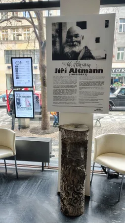 Výstavní panel s portrétem a textem o sochaři Jiřím Altmannovi a dřevěný reliéf
