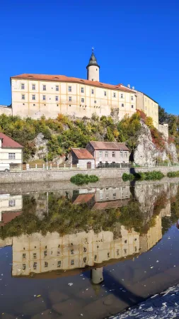Die Burg von Ledeč mit Turm auf dem Felsen über der Sázava und ihre Spiegelung im Wasser unter blauem Himmel