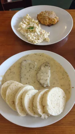 Teller mit Fleisch in Dillsauce und Semmelknödeln, daneben eine Schüssel Kartoffelsalat und ein Fleischpflanzerl