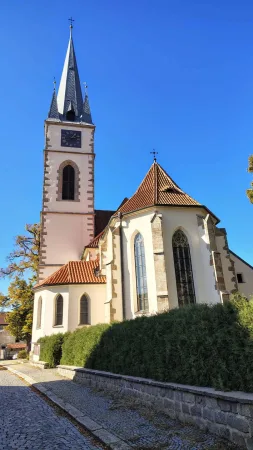 Kirche mit hohem, schlankem Turm mit Uhr und einer grünen Heckenwand in Ledeč nad Sázavou