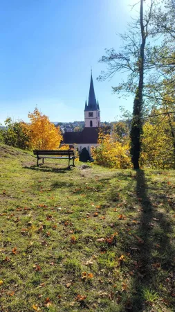Bank auf einer herbstlichen Wiese mit Blick auf den Kirchturm und gelb gefärbte Bäume