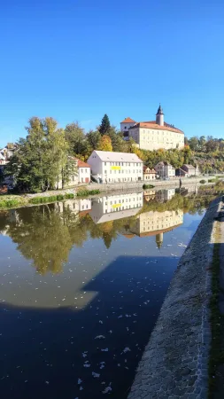 Die Burg von Ledeč auf dem Hügel über der Sázava mit Spiegelung in der ruhigen Wasserfläche und herbstlichen Bäumen