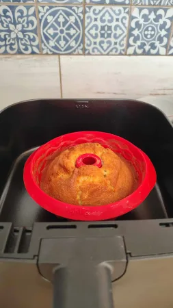 Zlatavě upečená malá bábovka v červené silikonové formě uvnitř šuplíku horkovzdušné fritézy