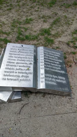 Detail bronzové sochy otevřené knihy s vytesaným polským textem o historii města.