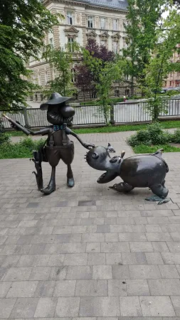 Bronzová socha lovce Pampalini v klobouku spolu s hrochem v parku.