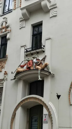 Sochy dvou žab hudebníků zdobící fasádu domu nad vchodem.