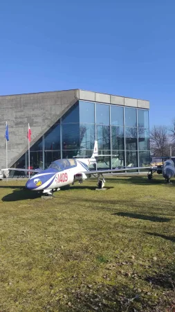 Modrobílé cvičné letadlo na trávníku před prosklenou budovou Muzea polského letectví v Krakově.