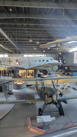 Rozlehlý hangár muzea letectví s několika historickými letadly včetně kamuflovaného dvouplošníku.