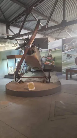 Historické letadlo s dřevěnou vrtulí vystavené před válečným dioramatem v muzeu.