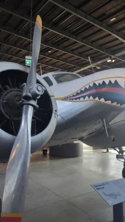 Vrtule v popředí a letoun Cessna s malovanou žraločí tlamou na přídi v hangáru.