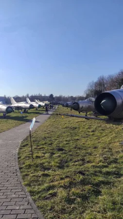 Řada stříbrných stíhacích letounů podél chodníku ve venkovní expozici muzea letectví.