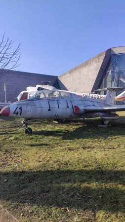 Vojenský cvičný letoun Aero L-29 Delfin vystavený venku na trávě v muzeu letectví.