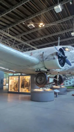 Velký historický transportní letoun s vrtulemi zavěšený v tmavém hangáru muzea letectví.