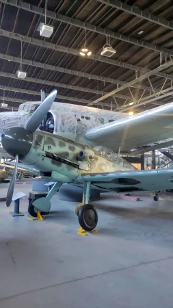 Kamuflovaný stíhací letoun Messerschmitt Bf 109 vystavený v hangáru muzea letectví.