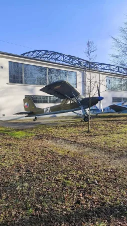 Malé vojenské letadlo s číslem 1101 a českou vlajkou vystavené na trávníku před budovou muzea.