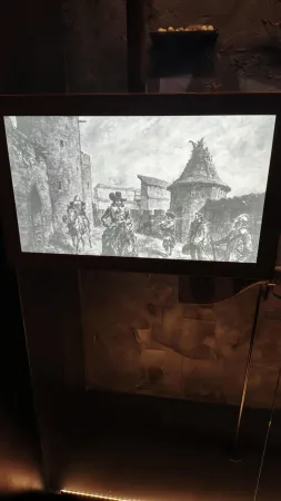 Černobílá historická ilustrace vojáků projíždějících opevněnou hradební branou