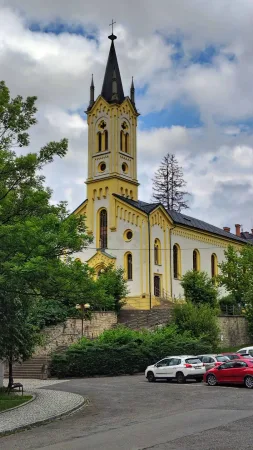 Žlutý evangelický kostel s vysokou věží obklopený zelení ve Vsetíně