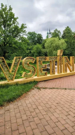 Zlatý nápis VSETÍN v parku s věží kostela v pozadí