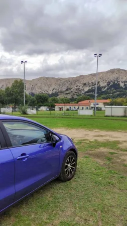 Naše modré auto zaparkované na hřišti s výhledem na hory v pozadí