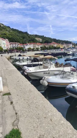 Kotviště lodí podél kamenného mola s domy a kopcem v pozadí