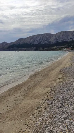 Klidná oblázková pláž s tyrkysovým mořem a horami v pozadí