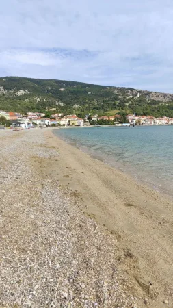 Pískovo-kamínková pláž s výhledem na městečko Baška a okolní hory
