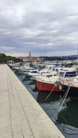Kamenná promenáda podél přístavu s loděmi a věží města Krk